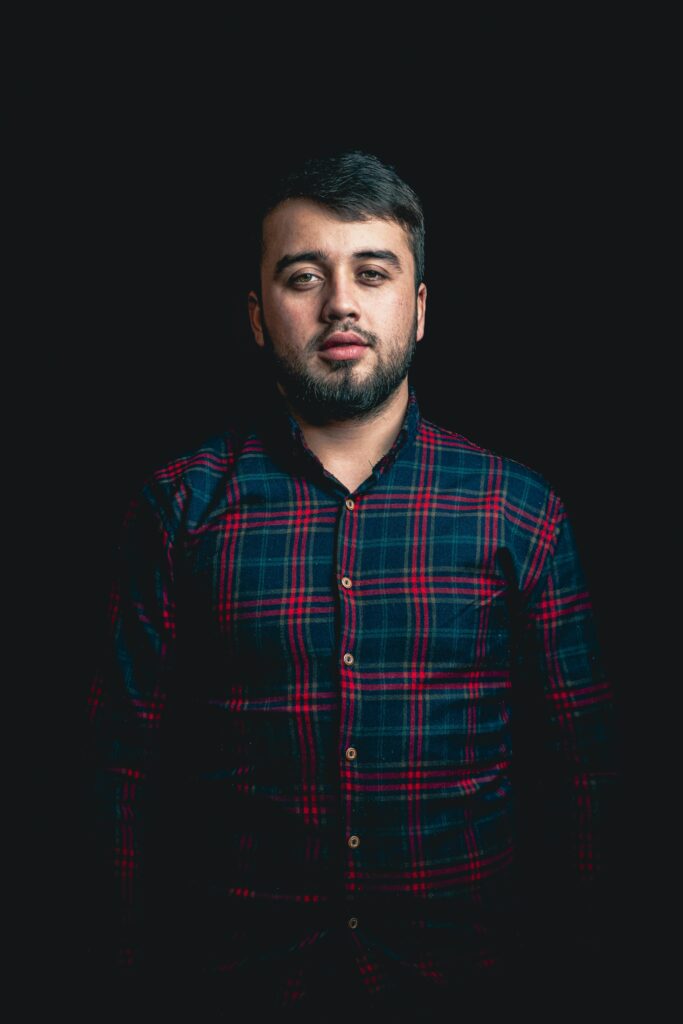 Fashion portrait of a man in a checkered shirt with a dark background, showcasing casual style.